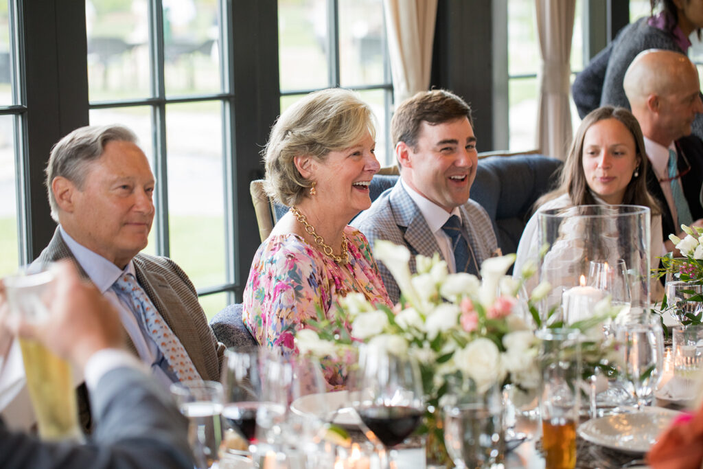 A mother, father, son and daughter-in-law sitting at a table decorated with pink and white florals.