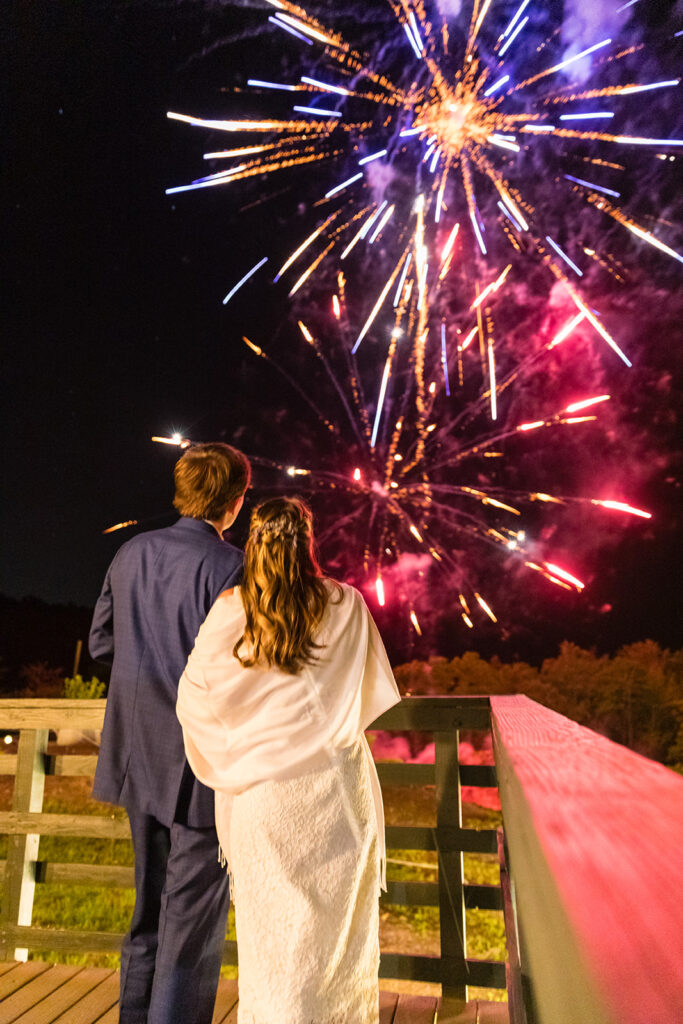 A bride and groom standing together on a porch watching fireworks at Skyline Lodge in Highlands, North Carolina. 