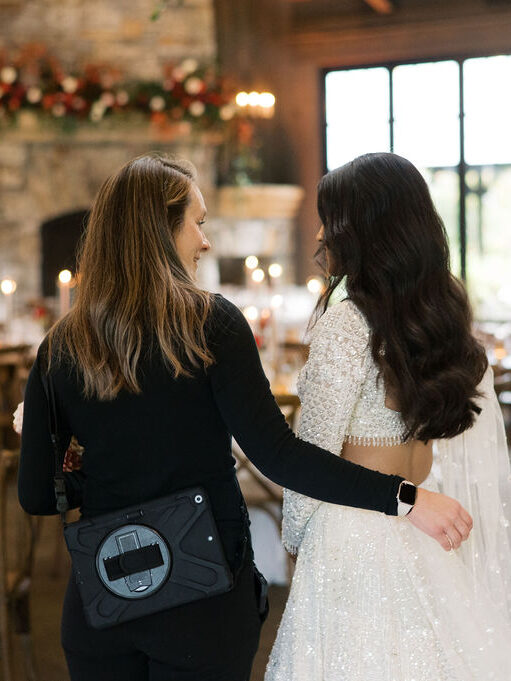 Two women, one dressed in black and the other in a wedding dress, standing with their backs to the camera talking.