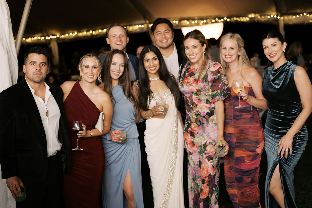 A group of 10 people at a wedding rehearsal dinner, holding drinks and smiling together at Old Edwards Inn in Highlands, North Carolina. 