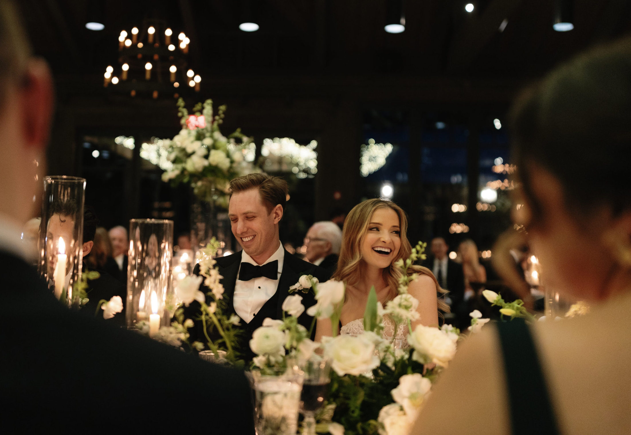 bride and groom smiling and sitting at a table with candles and white flowers at Old Edwards Inn in Highlands, North Carolina.